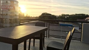 A rooftop terrace with a table and chairs, a water tank labeled "BESTANK", and a sunset in the background. - Life In Santa Maria (Santa Maria)