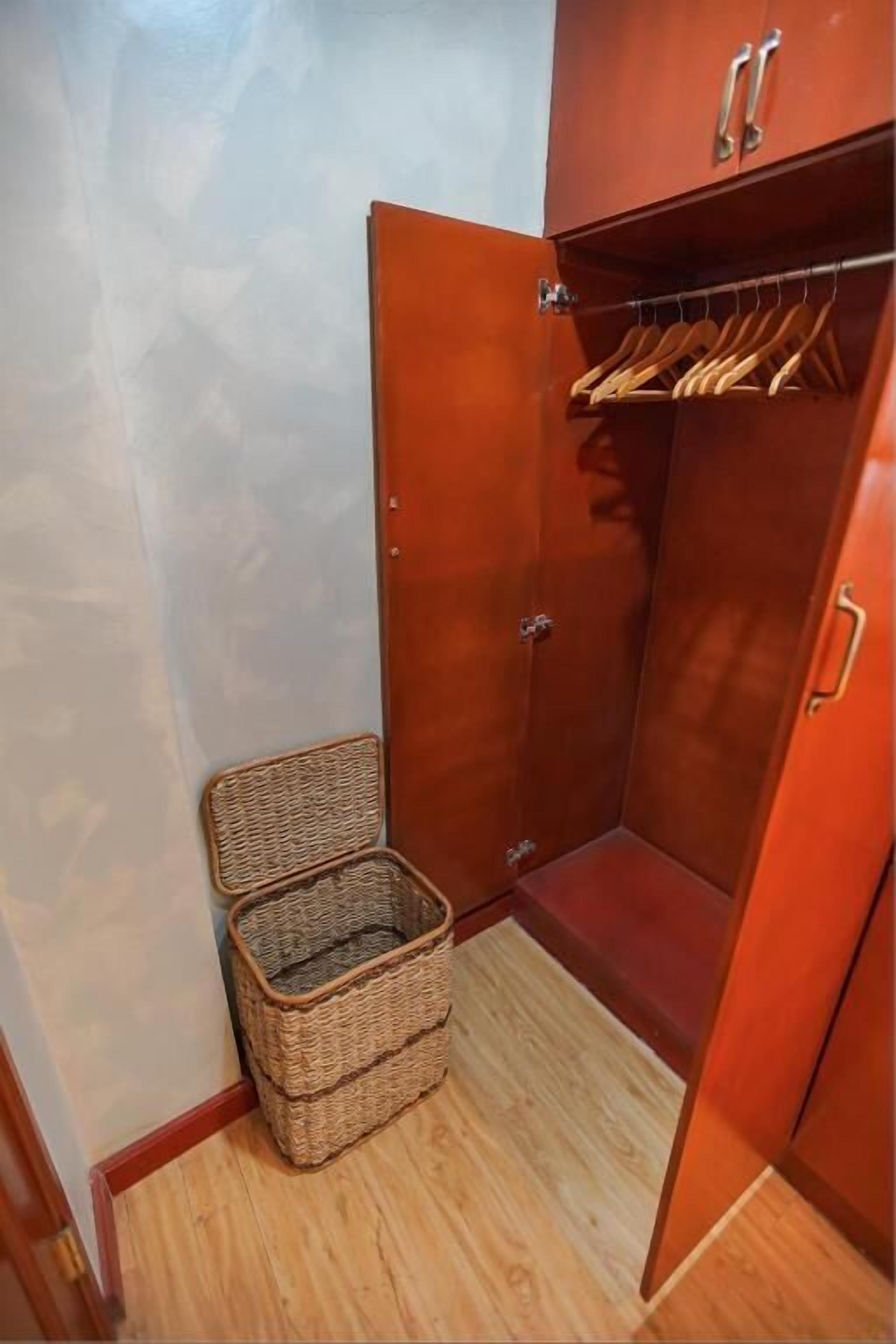 A wooden closet with a hanging rod and a wicker basket.