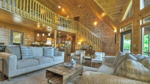 Interior de una cabaña con sala de estar, cocina y una escalera que lleva a una terraza superior.