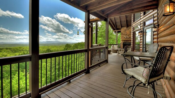 Una terraza de madera con mobiliario exterior y vistas a un paisaje boscoso.