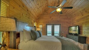 Un dormitorio de cabaña de madera con una cama, almohadas, un televisor y un ventilador de techo.