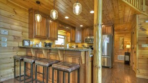 Interior de una cabaña de madera con cocina, que incluye armarios de madera, un refrigerador de acero inoxidable y una barra con taburetes.
