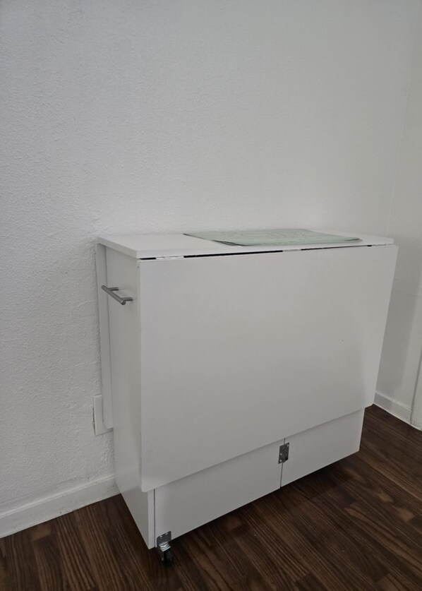 A white cabinet with a flat-screen TV on top, positioned against a white wall with a wooden floor.