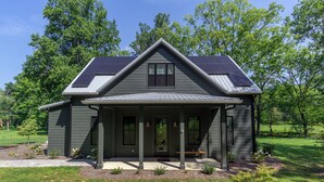 Une maison moderne dotée de panneaux solaires, d’un porche abrité et d’une bordure en pierre autour de la pelouse.