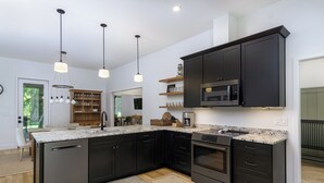 Une cuisine moderne avec des meubles de couleur sombre, un four à micro-ondes encastré et un grand îlot central doté d’un évier.