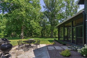 A patio with stone flooring, a grill, and outdoor furniture. - Creek Song | Energy Efficient, Fire Pit & Creek Access! (Fairview)