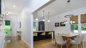 Une cuisine moderne dotée d’un grand îlot central, de luminaires suspendus et d’un coin repas avec une table et des chaises en bois.