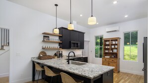 Une cuisine moderne dotée d’un grand îlot central, de tabourets de bar, de luminaires suspendus et offrant une vue sur l’extérieur.