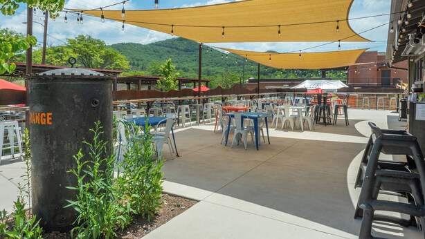An outdoor seating area with tables and chairs, a large planter, and a building in the background. - Cherry Street Loft (A) | In the Heart of Downtown Black Mtn! (Black Mountain)