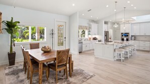 A modern kitchen with white cabinets, a central island with bar stools, and a dining area with a wooden table and chairs. - New Listing! Luxury 4BR Canal Home with Pool. Monthly Rental.    (Holmes Beach)