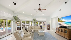 A spacious living room with a sectional sofa, a coffee table, and a television displaying a beach scene. - New Listing! Luxury 4BR Canal Home with Pool. Monthly Rental.    (Holmes Beach)