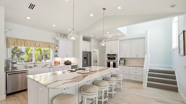A modern kitchen with a large island, bar stools, and a staircase leading to another level. - New Listing! Luxury 4BR Canal Home with Pool. Monthly Rental.    (Holmes Beach)
