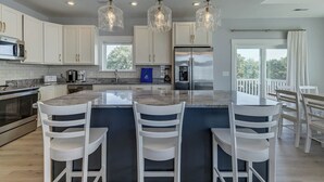 Een moderne keuken met witte kasten, een centraal eiland met barkrukken, roestvrijstalen apparatuur en hangende lampen.