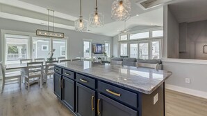 Een moderne keuken met een groot schiereiland, hangende lampen en uitzicht naar buiten.