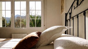 A bed with white and brown pillows, a window with a view of mountains, and a black metal headboard. - Vivienda Vacacional El Cuetu del Sella (Llames De Pria)
