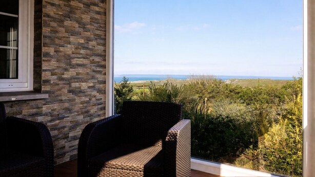 A balcony with wicker chairs, a stone wall, and a view of the sea. - Vivienda Vacacional El Cuetu del Sella (Llames De Pria)