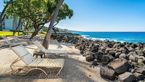 A beach with sun loungers, palm trees, and a rocky shoreline. - 🏖️Pretty Ocean View | Top Floor | Concierge Included (Kailua Kona)