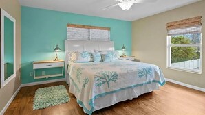 Quarto com cama, mesas de cabeceira, ventoinha no teto e janela com persianas.