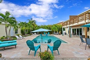 A swimming pool with lounge chairs and umbrellas, surrounded by palm trees and a covered patio area. - Tropical Haven A - 4503   “Anna Maria Island” (Bradenton)