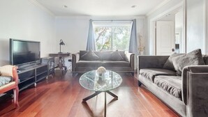 Un salon comprenant un téléviseur à écran plat, une table basse ronde en verre, un canapé et une causeuse.