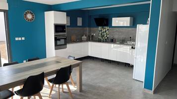 Une cuisine moderne avec des armoires blanches, un four encastré et un four à micro-ondes. On y trouve une table à manger avec des chaises et un mur d’accent bleu.