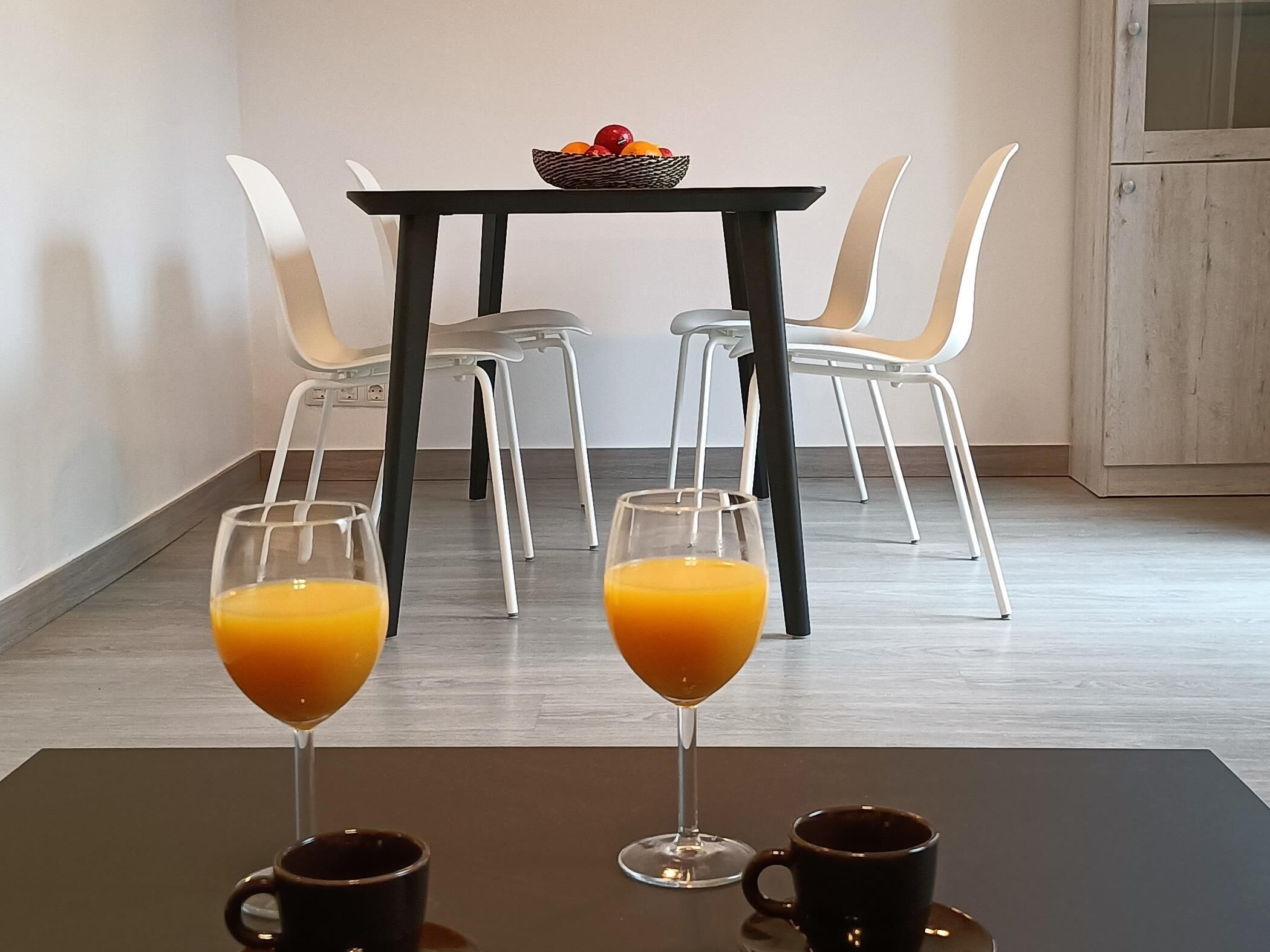 A dining area with a table, four chairs, two glasses of orange juice, and two coffee cups.