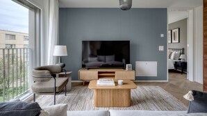 Una sala de estar moderna con un televisor de pantalla plana grande, un sofá, una mesa de centro y una silla.