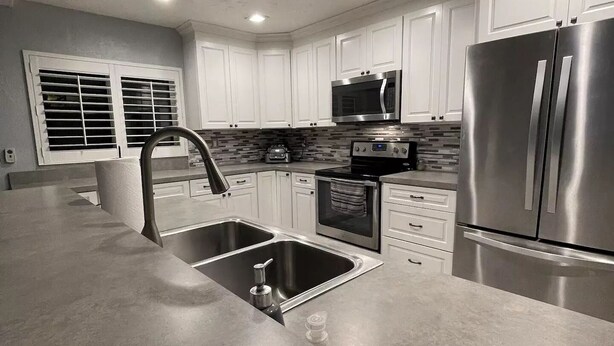 A modern kitchen with white cabinets, stainless steel appliances, and a large island with a sink. - Pacifico Blu Guest House- close to beaches! (Clearwater)
