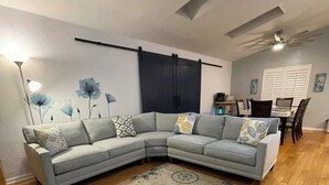 A living room with a light grey sectional sofa, a patterned rug, and a dining area with a table and chairs. - Pacifico Blu Guest House- close to beaches! (Clearwater)