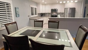 A modern kitchen with white cabinets, stainless steel appliances, and a glass-top dining table surrounded by chairs. - Pacifico Blu Guest House- close to beaches! (Clearwater)