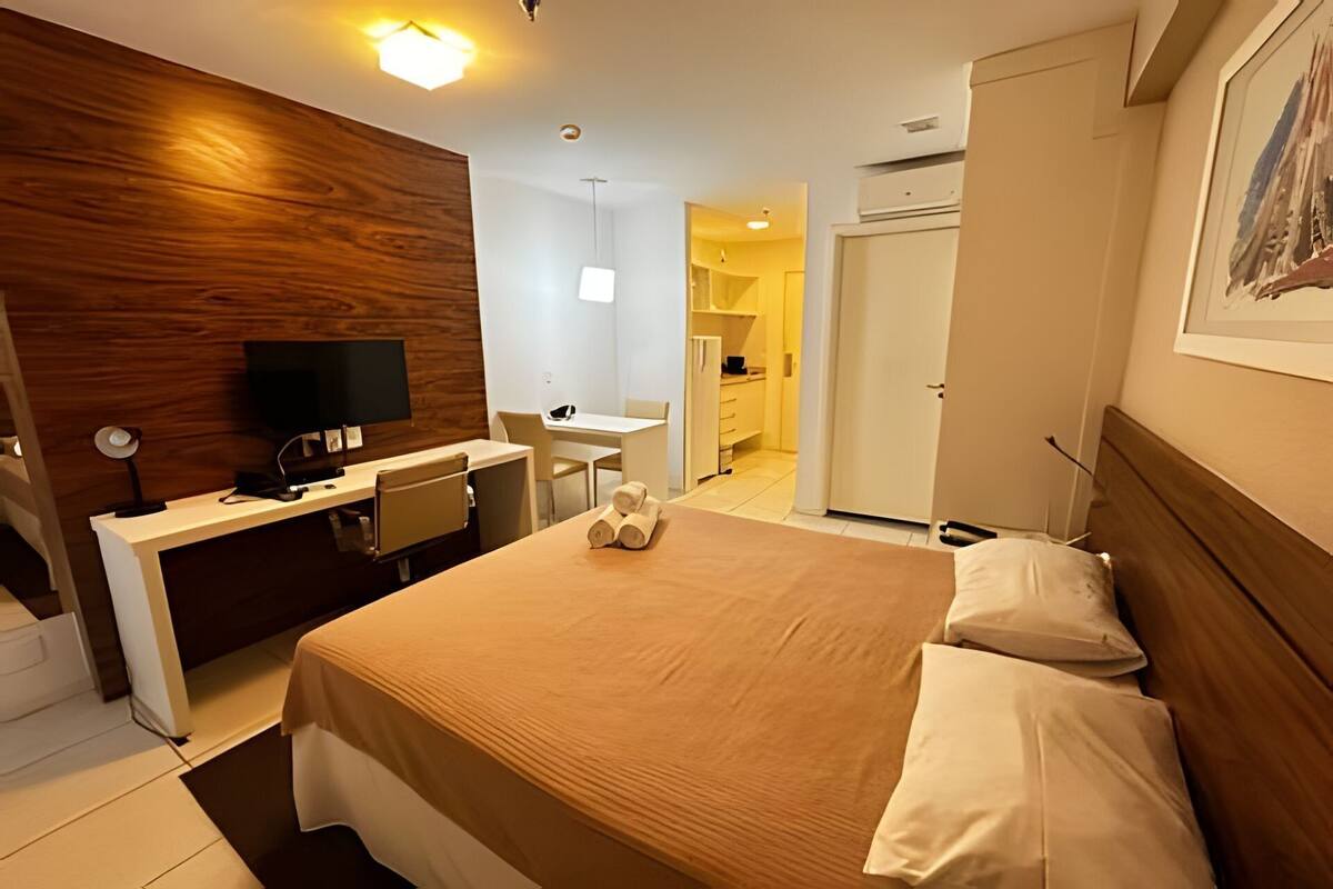 Een hotelkamer met een wand van hout, een bureau met computer, een bed met witte lakens en een schilderij aan de muur.