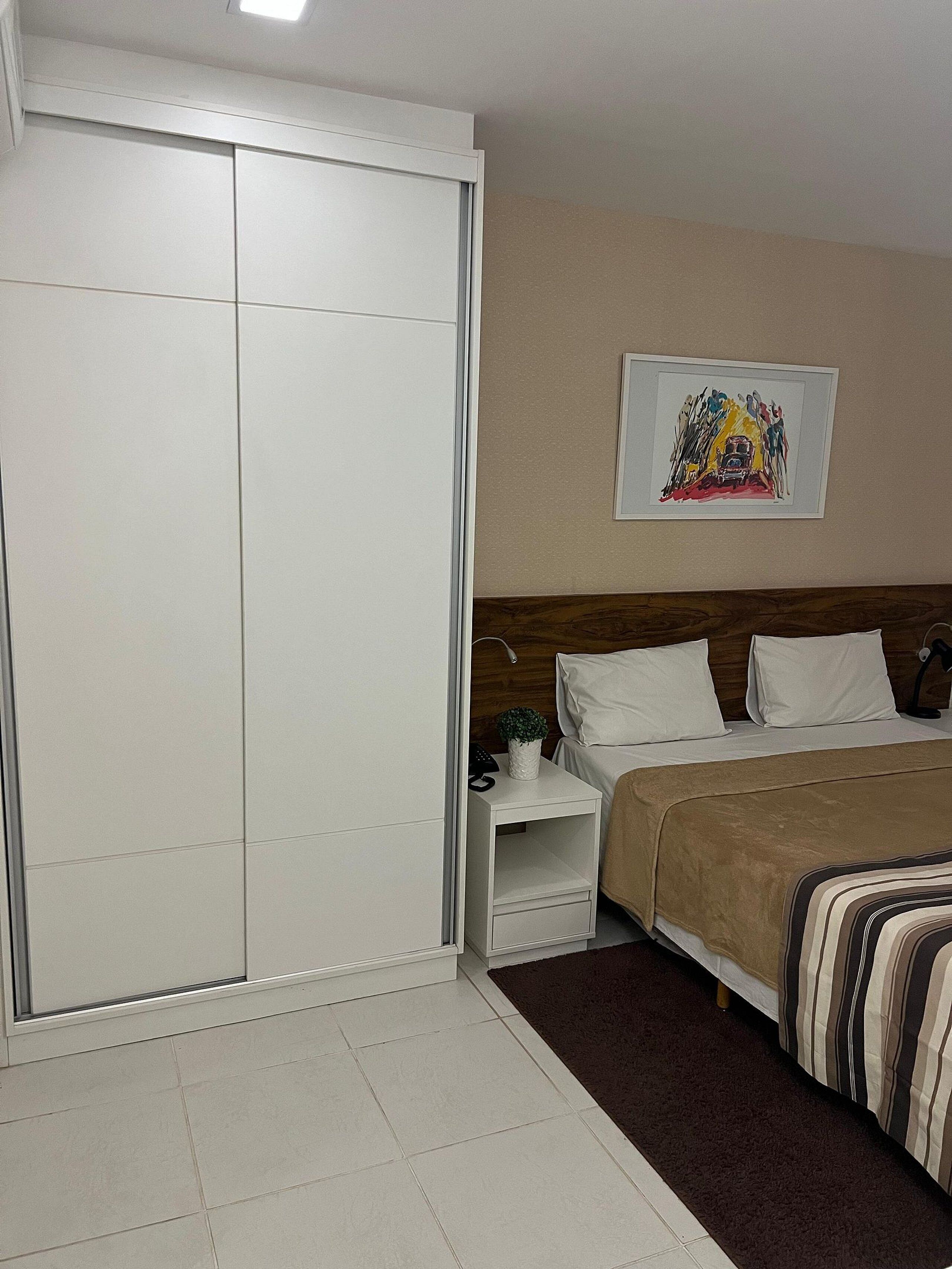 A bedroom with a bed, bedside tables, a wardrobe, and a wall-mounted artwork.