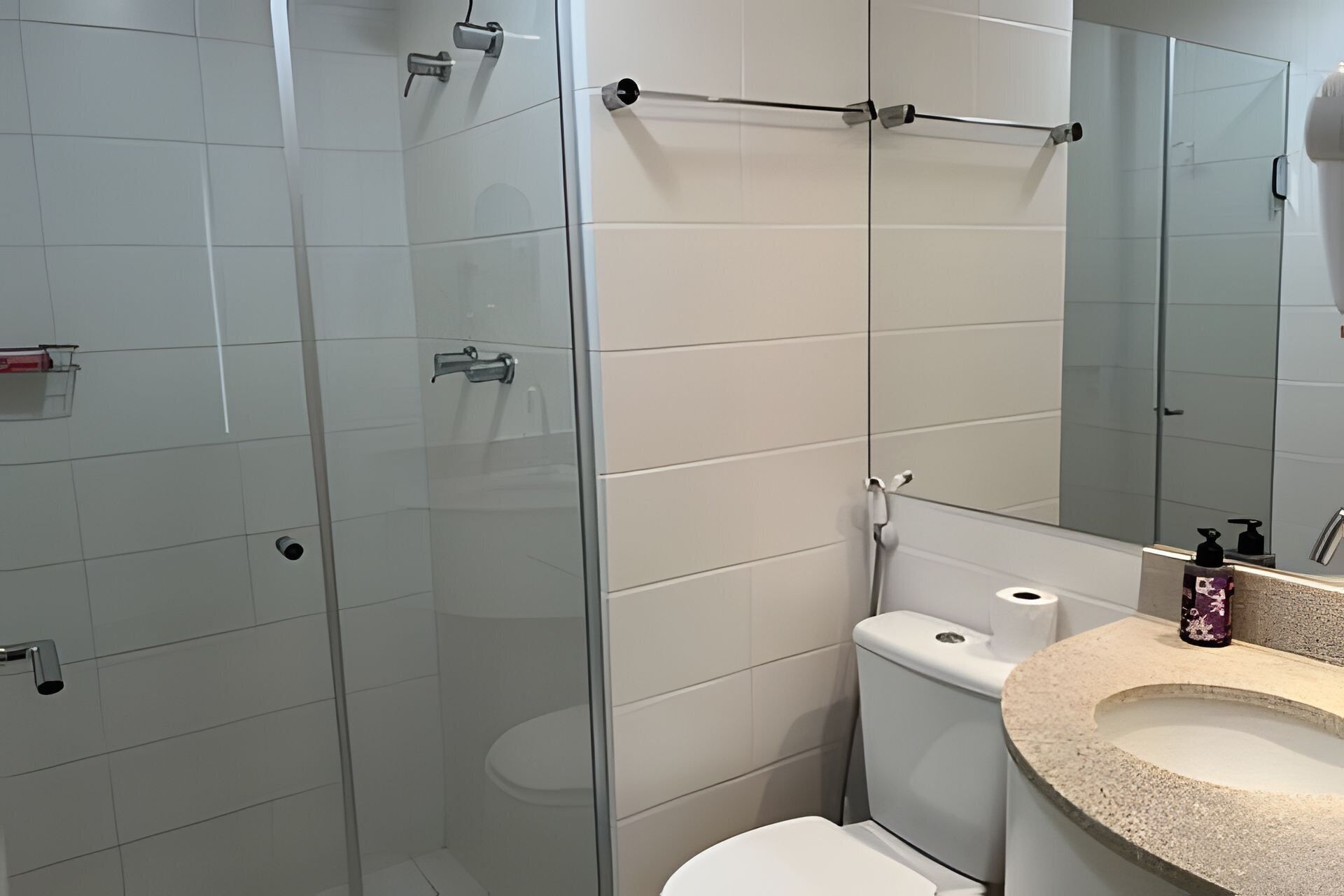 Ein modernes Badezimmer mit Duschkabine aus Glas, Toilette und Waschbecken mit Spiegel darüber.