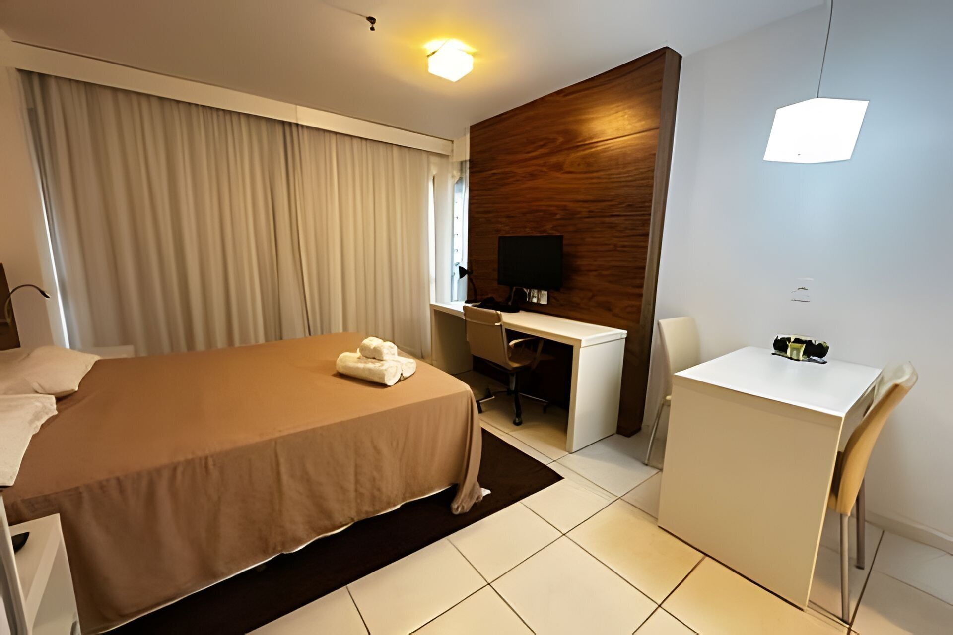 A hotel room with a bed, a desk, a chair, a TV, and a small table.