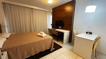 A hotel room with a bed, a desk, a chair, a TV, and a small table.