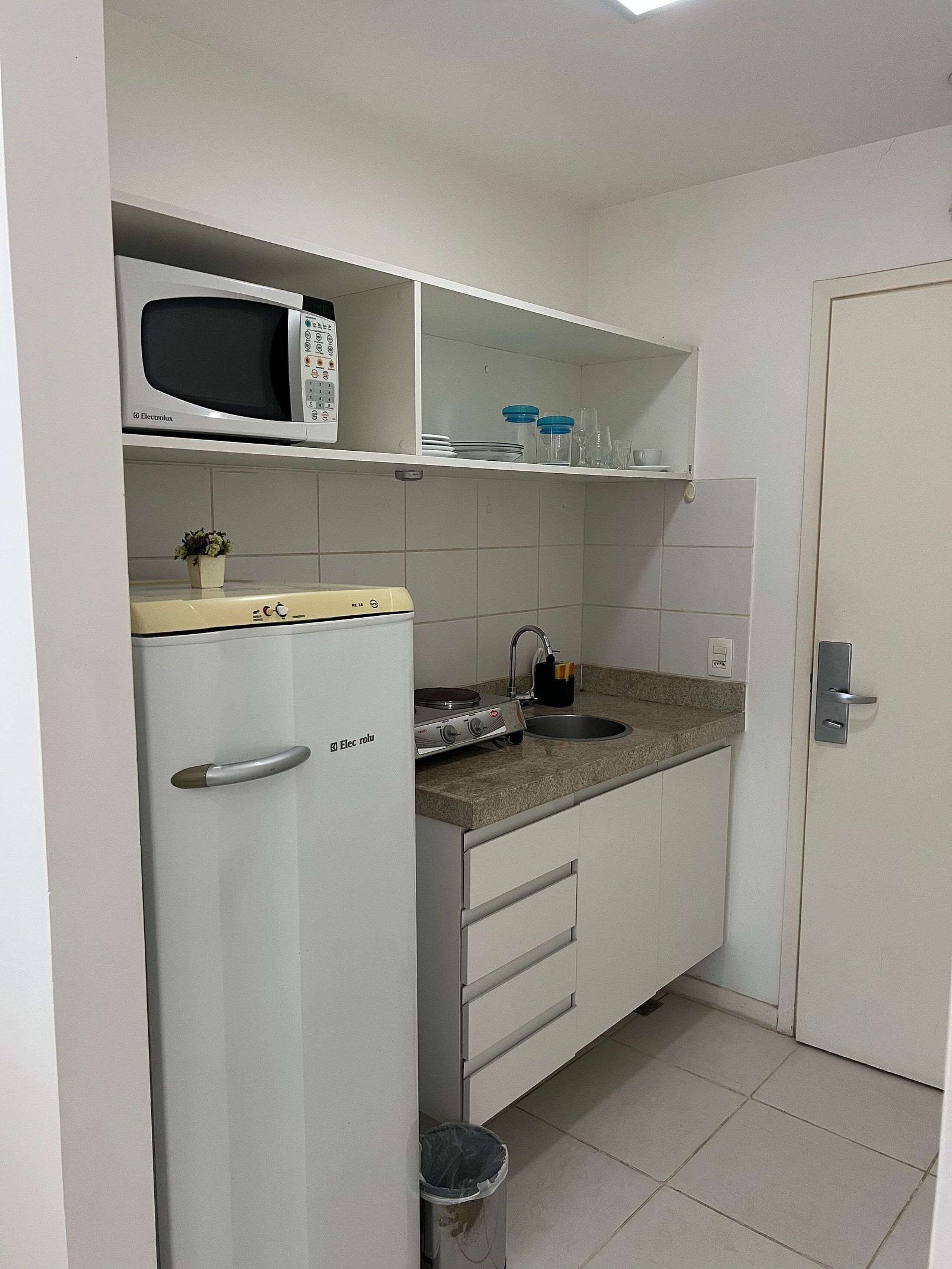 Een functionele keuken met een magnetron, kookplaat, spoelbak en een kleine potplant.