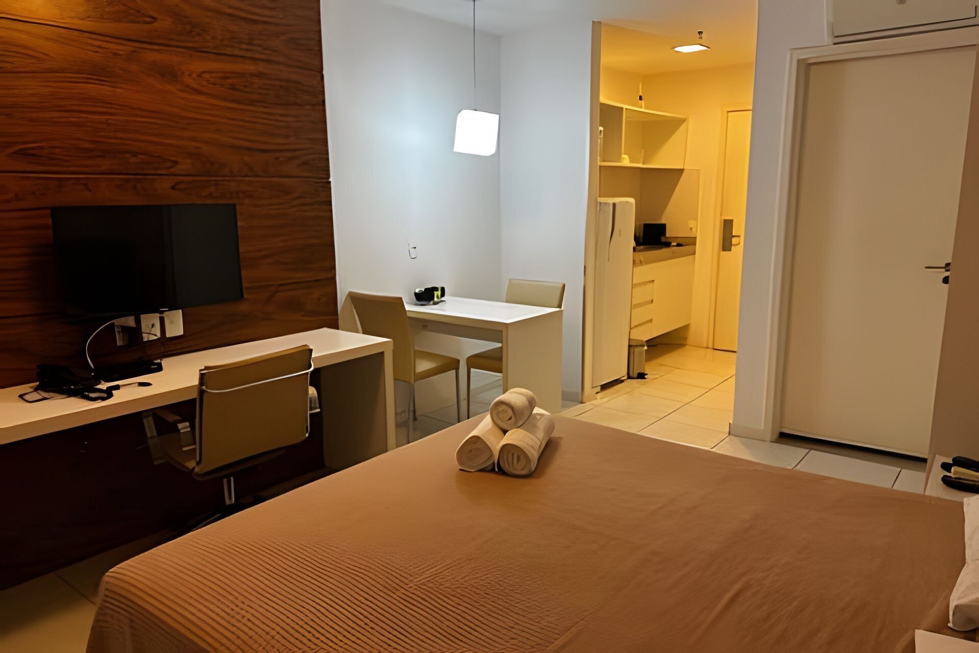 A hotel room with a bed, a desk with a chair, a television, and a kitchenette.