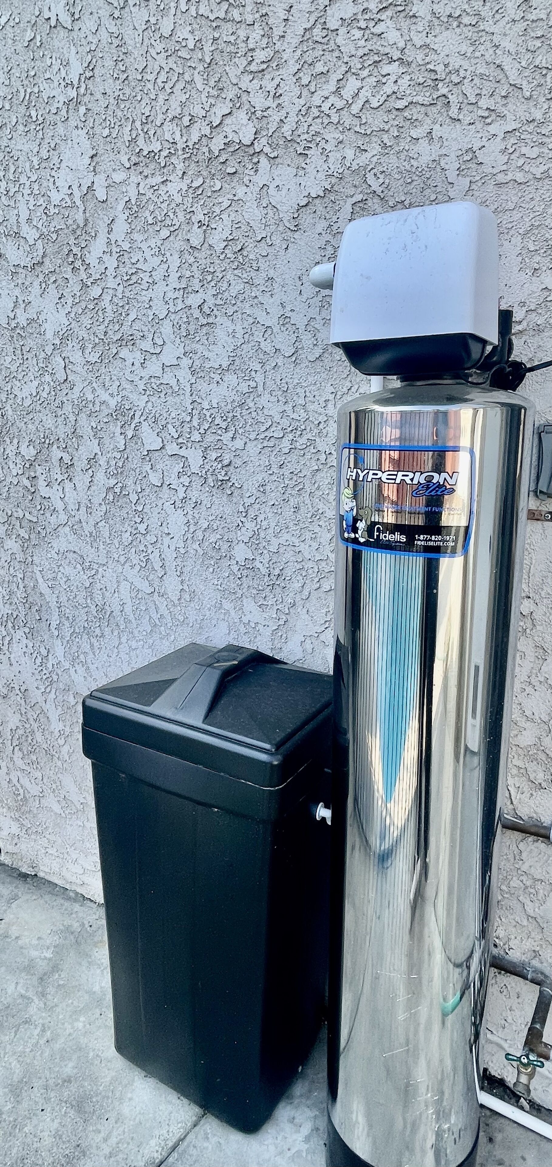 A metallic vending machine with a label and a black trash bin beside it.