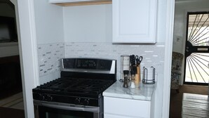 Una cucina compatta con piano cottura a gas, forno e mobili bianchi.