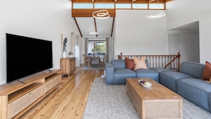 Un salón amplio con televisor grande, suelo de madera, un sofá azul y una escalera.