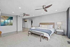 Ein modernes Schlafzimmer mit einem großen Bett, zwei Deckenventilatoren, einer Bank und einem Bild an der Wand.