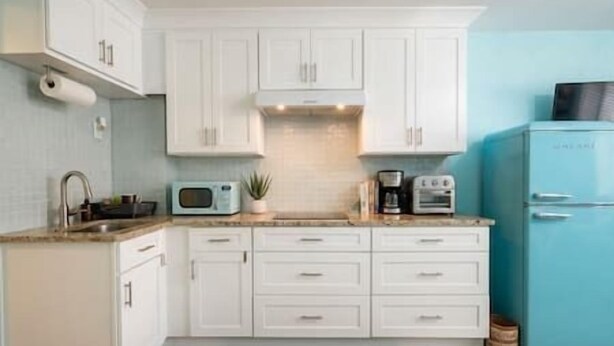 Una cocina con armarios blancos, un microondas, una cafetera y un refrigerador azul.