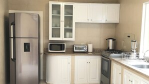 Una cocina con armarios blancos, un refrigerador de acero inoxidable, un microondas, un tostador, una estufa y un lavamanos.