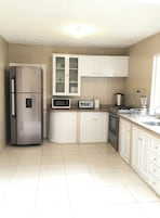 Una cocina con armarios blancos, un refrigerador de acero inoxidable, un microondas, un tostador, una estufa y un lavamanos.