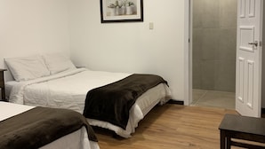 Un dormitorio con dos camas, piso de madera, una puerta blanca y un cuadro enmarcado en la pared.