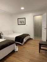 Un dormitorio con dos camas, piso de madera, una puerta blanca y un cuadro enmarcado en la pared.