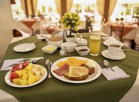 Un desayuno con tostadas, huevos, fruta, una taza de café y un vaso de jugo.