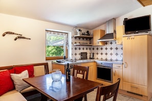 A compact kitchen with a dining area, a window with a view, and a TV mounted on the wall.