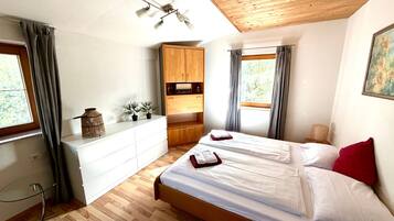 A bedroom with a wooden bed, a white dresser, a wooden wardrobe, and a window with curtains.