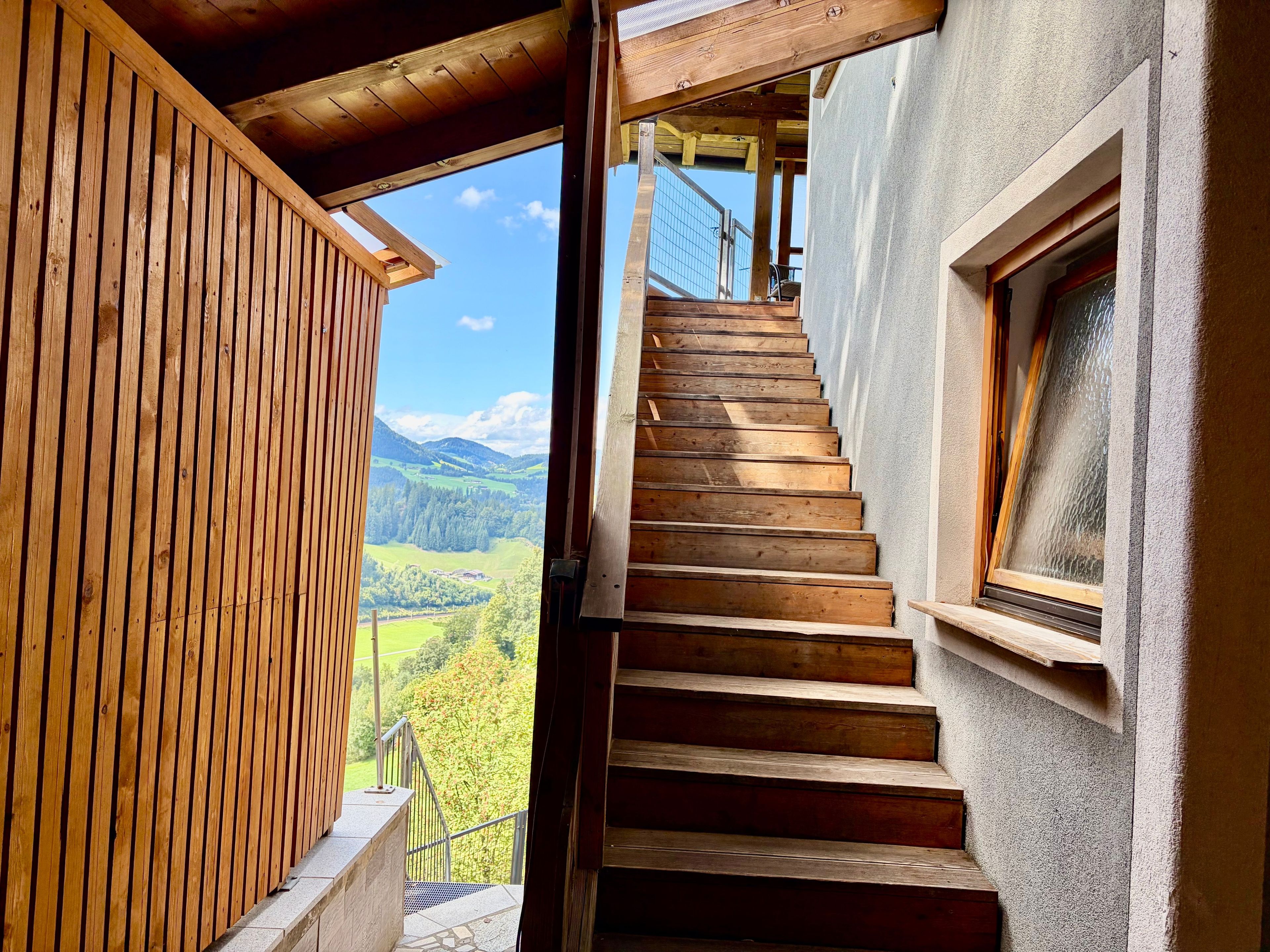 A wooden staircase leading to a balcony with a view of a mountainous landscape.